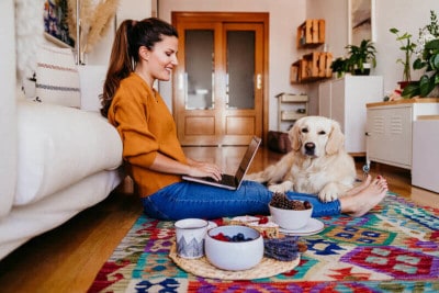 Young woman working on laptop with cute golden retriever dog.
